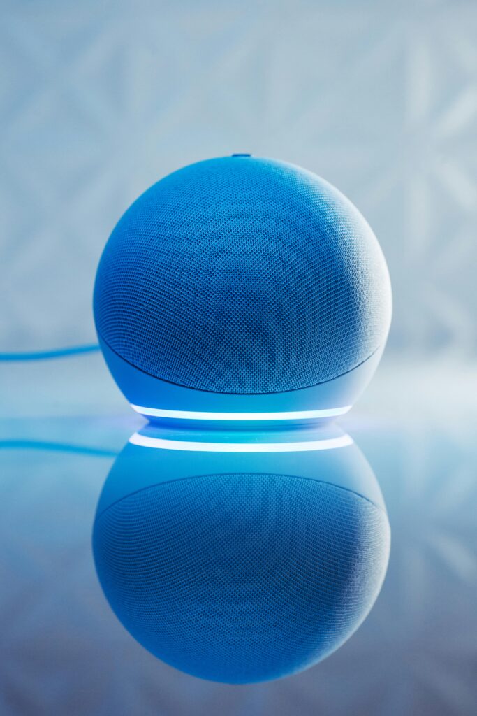 A smart speaker with glowing blue LED lighting and its reflection on a surface.